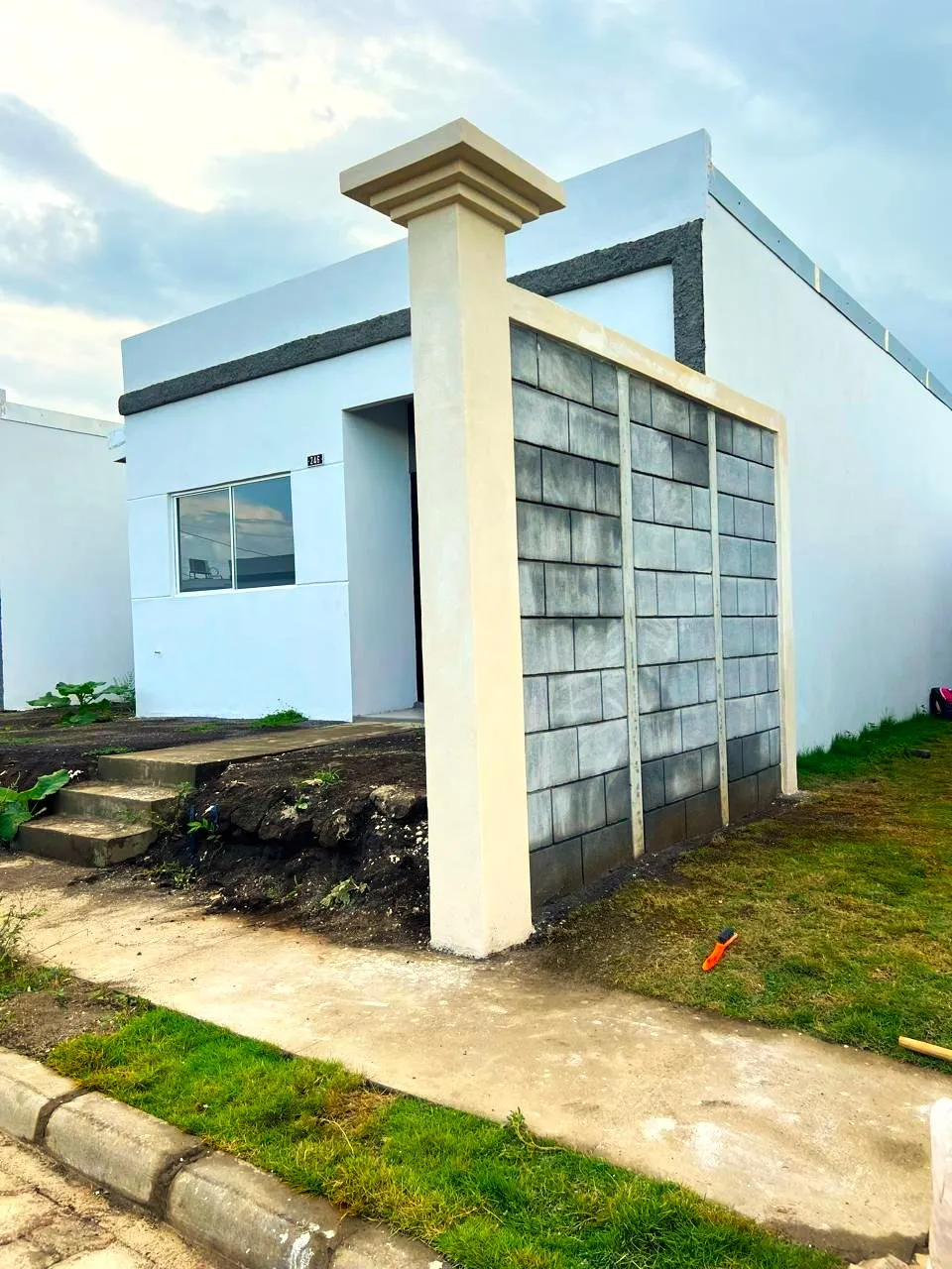 Sección de muro frontal compuesto construido con el sistema prefabricado Maxiblock. Muestra un zócalo en la base que funciona como muro de contención para retener el cambio de altura entre la calle y la terraza del terreno, complementado con una columna estilizada de concreto armado diseñada para sostener el portón.