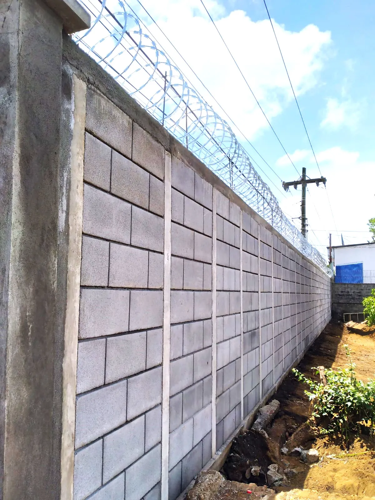 Muro perimetral de seguridad perimetral de gran altura construido con bloques prefabricados Maxiblock. Muestra columnas de concreto intermedias y una terminación superior reforzada con alambre de púas tipo concertina para máxima protección residencial o industrial.