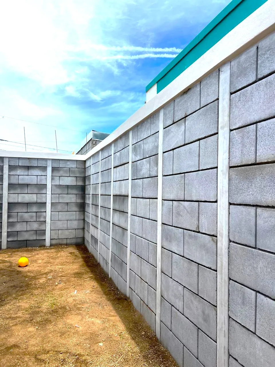 Vista interna de un patio residencial con cerramiento perimetral en esquina, edificado con el sistema modular de muros prefabricados Maxiblock. Destaca el acabado limpio de las uniones, las columnas de soporte gris claro y una viga corona superior.