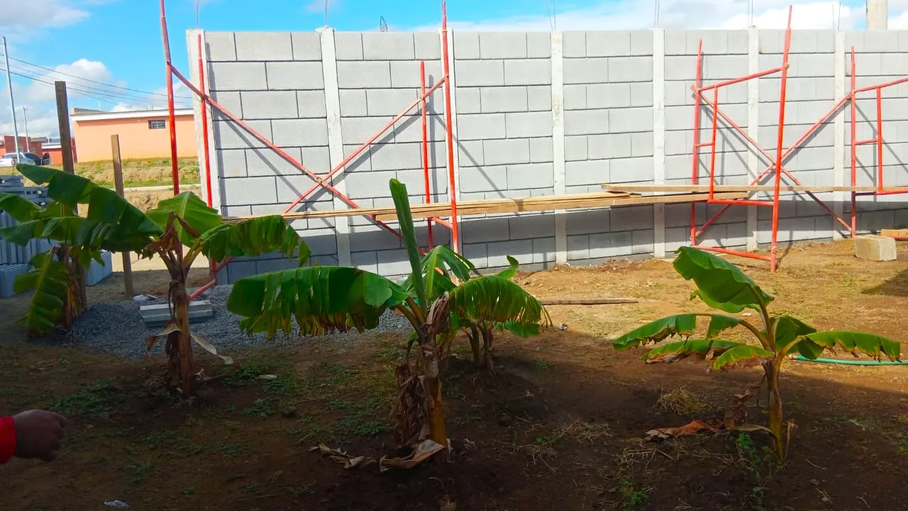 Proceso de construcción y ensamble de un muro perimetral de alta resistencia con el sistema prefabricado Maxiblock. Se observa la colocación de los bloques modulares a gran altura asistida por estructuras de andamios tubulares rojos.
