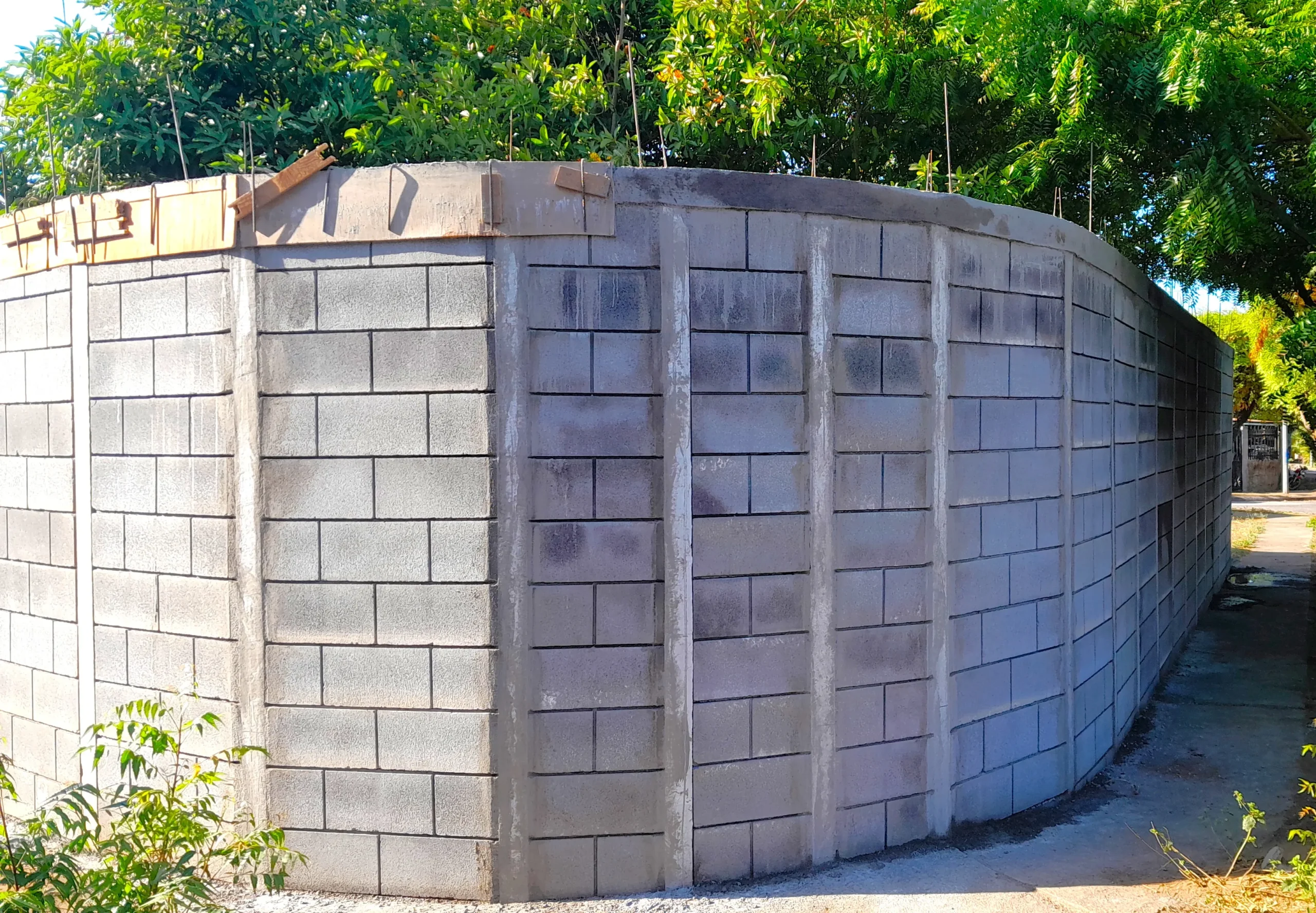 Vista en detalle del proceso de construcción de un muro perimetral curvo con bloques prefabricados del sistema Maxiblock, mostrando las columnas de concreto reforzado y la precisión estructural antes de la aplicación de los acabados finales.