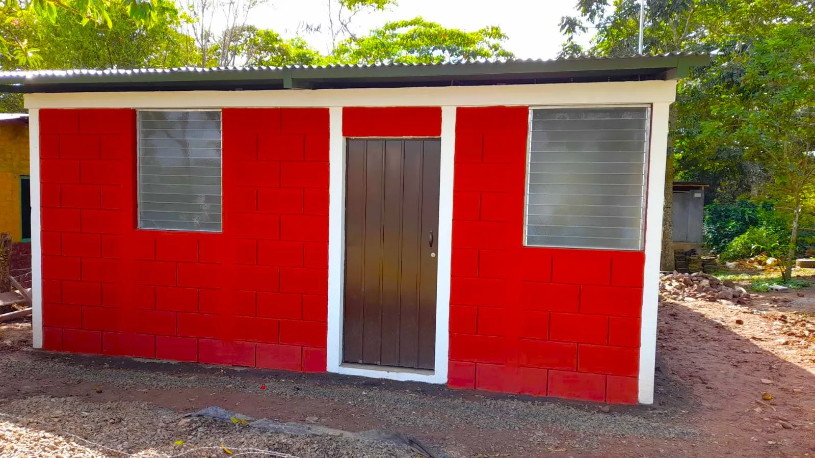 Exterior de viviendas prefabricadas nicaragua pintadas en rojo. Bloques Maxiblock, marcos blancos y puerta de madera bajo techo de lámina.