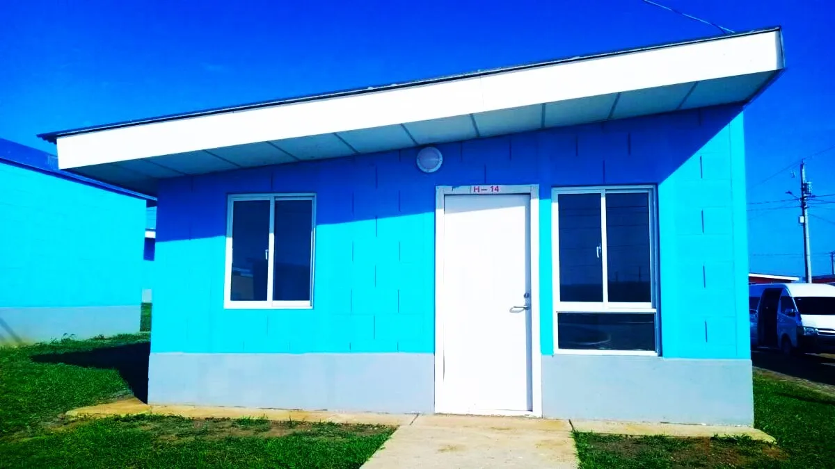 Fachada modelo M37 para viviendas prefabricadas nicaragua en tono azul. Techo con caída inclinada, puerta blanca y ventanas de aluminio.