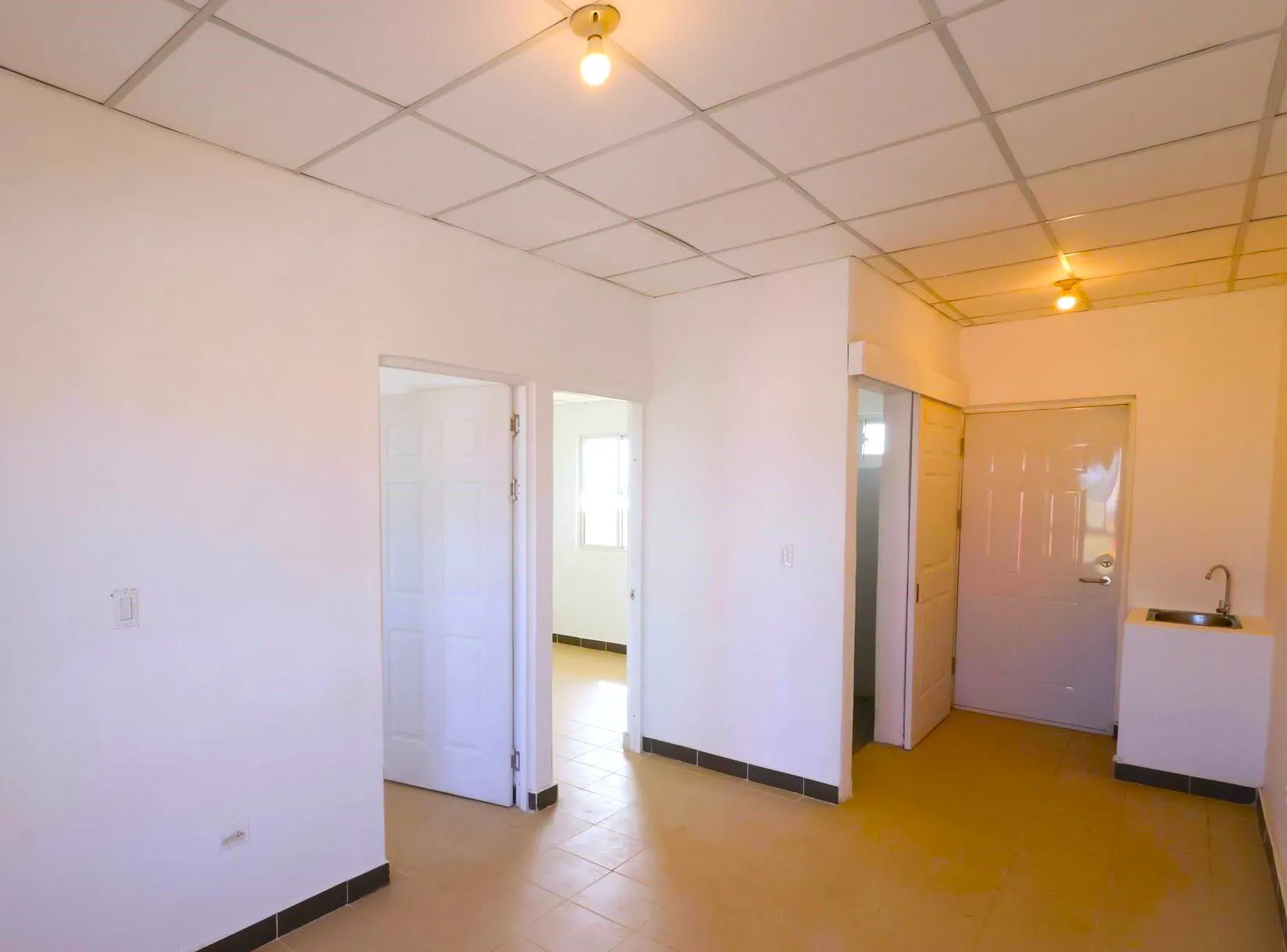 Interior de concepto abierto en viviendas prefabricadas nicaragua. Paredes lisas, piso cerámico beige y cocina con lavatrastos instalado.