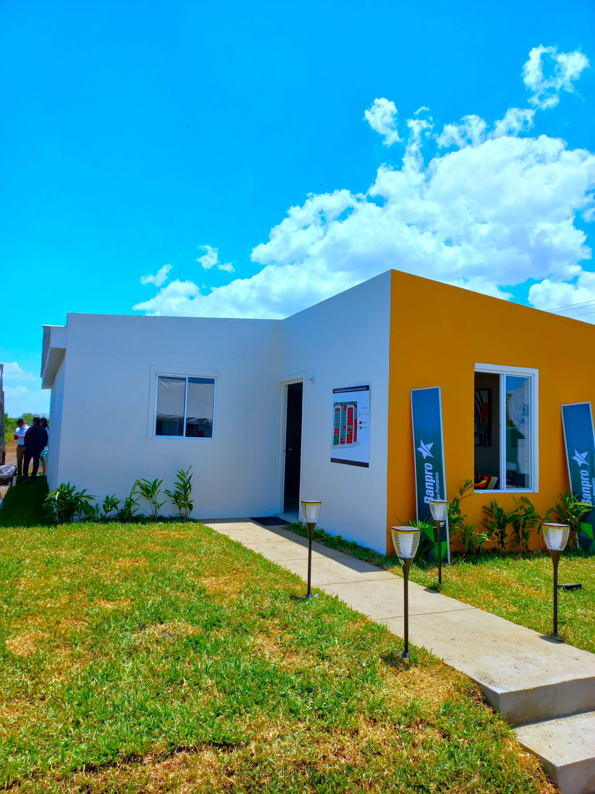 Fachada modelo Madroño para viviendas prefabricadas nicaragua. Diseño moderno en blanco y amarillo con jardín frontal y sendero de concreto.