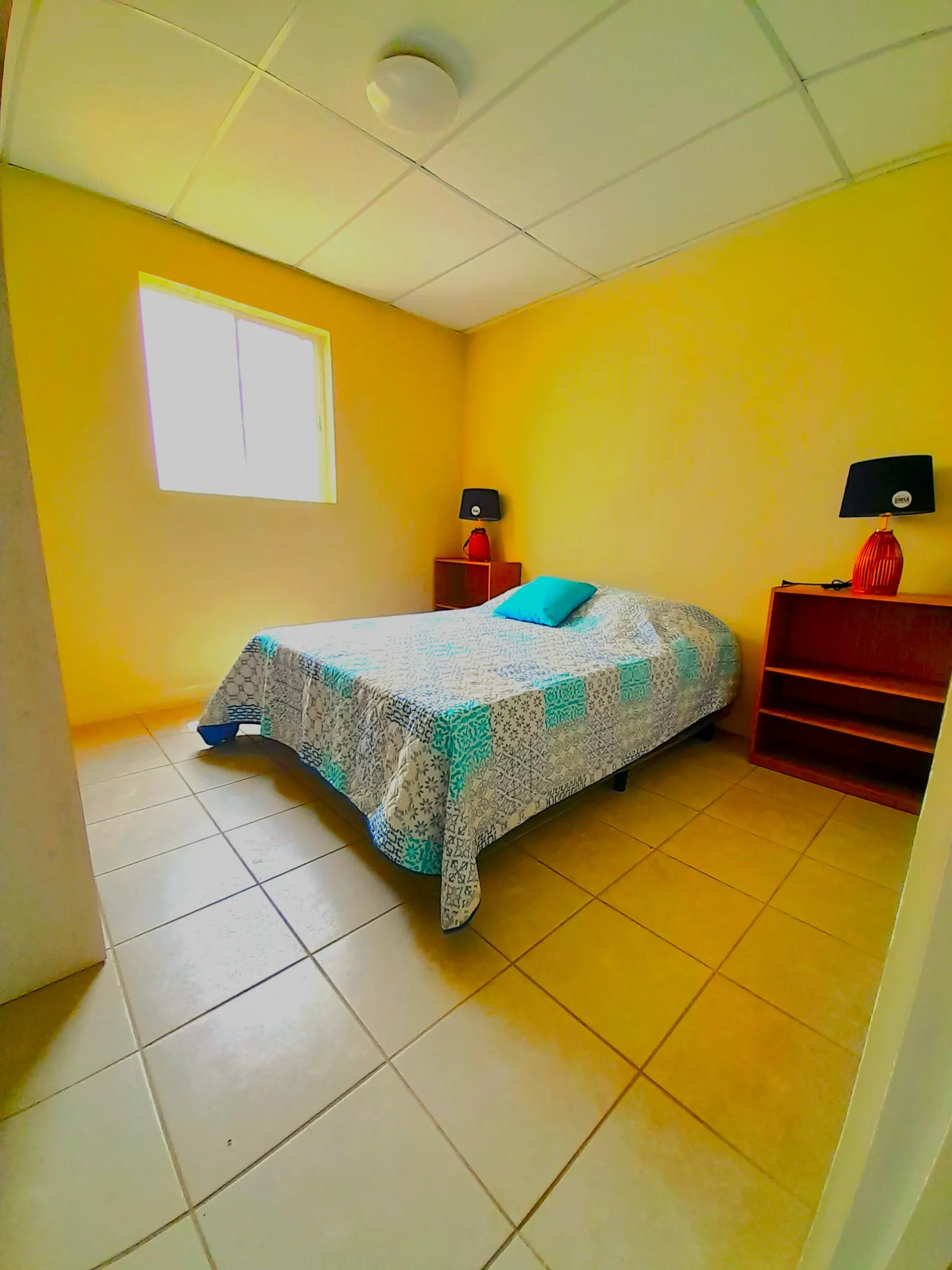 Dormitorio interior en viviendas prefabricadas nicaragua con Maxiblock. Paredes amarillas, piso cerámico, cielo falso y gran iluminación natural.