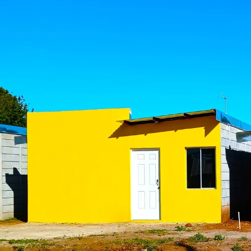 Fachada Blanca Arauz para viviendas prefabricadas nicaragua. Pared lisa amarilla y laterales de bloques grises Maxiblock expuestos.