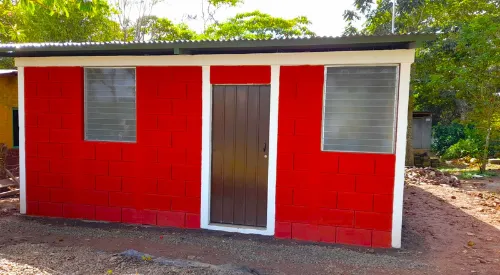 Exterior de viviendas prefabricadas nicaragua pintadas en rojo. Bloques Maxiblock, marcos blancos y puerta de madera bajo techo de lámina.