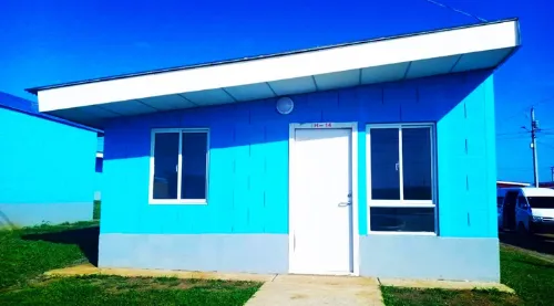Fachada modelo M37 para viviendas prefabricadas nicaragua en tono azul. Techo con caída inclinada, puerta blanca y ventanas de aluminio.
