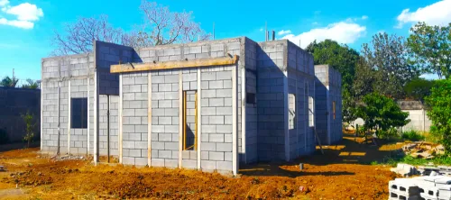 Vista exterior de viviendas prefabricadas nicaragua en construcción con Maxiblock. Paredes modulares grises y columnas integradas en el terreno.