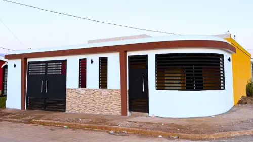Fachada frontal residencial moderna construida con el sistema prefabricado Maxiblock, con acabados en pintura blanca, molduras marrón oscuro y portón negro de seguridad.