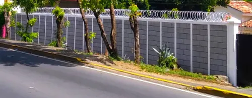 Muro perimetral frontal de alta resistencia construido con el sistema de cerramiento prefabricado Maxiblock, con protección superior de serpentina.