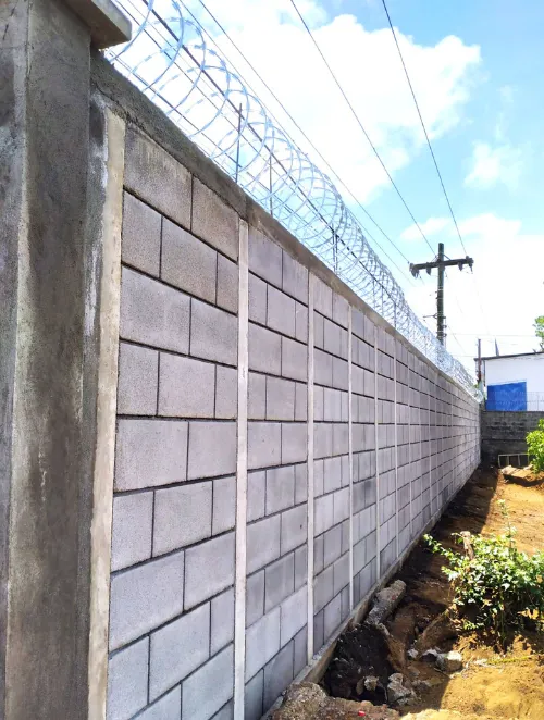 Vista interior de un patio residencial con muro de seguridad perimetral de Maxiblock y protección de concertina.